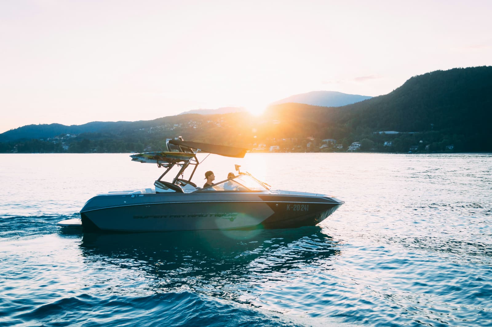 Wakeboard boat at sunset on calm lake with mountain backdrop