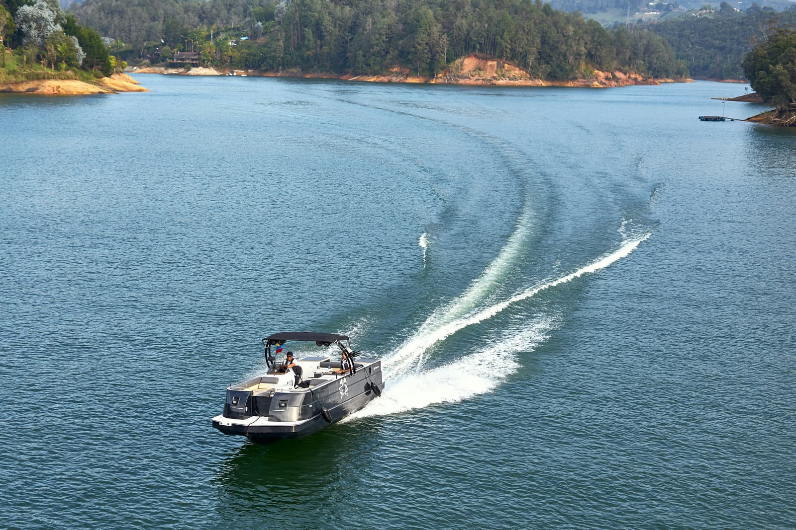 Pontoon boat cruising on a lake with wooded shoreline