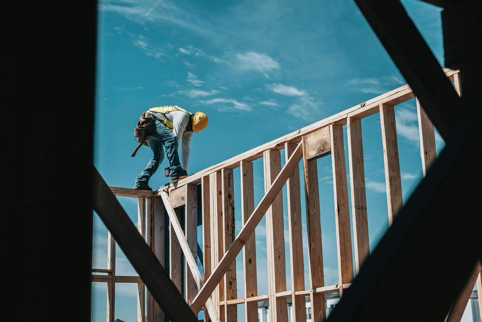 Construction worker framing a residential building against a bright blue sky