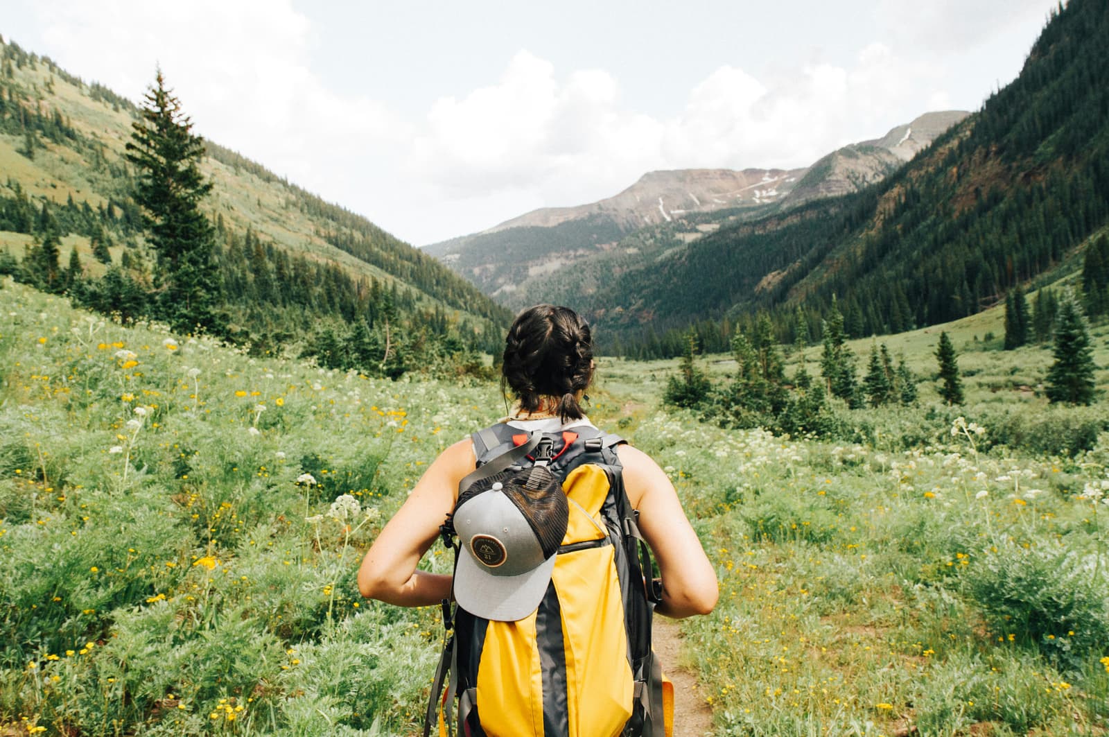 Hiker with yellow backpack walking through a lush mountain meadow