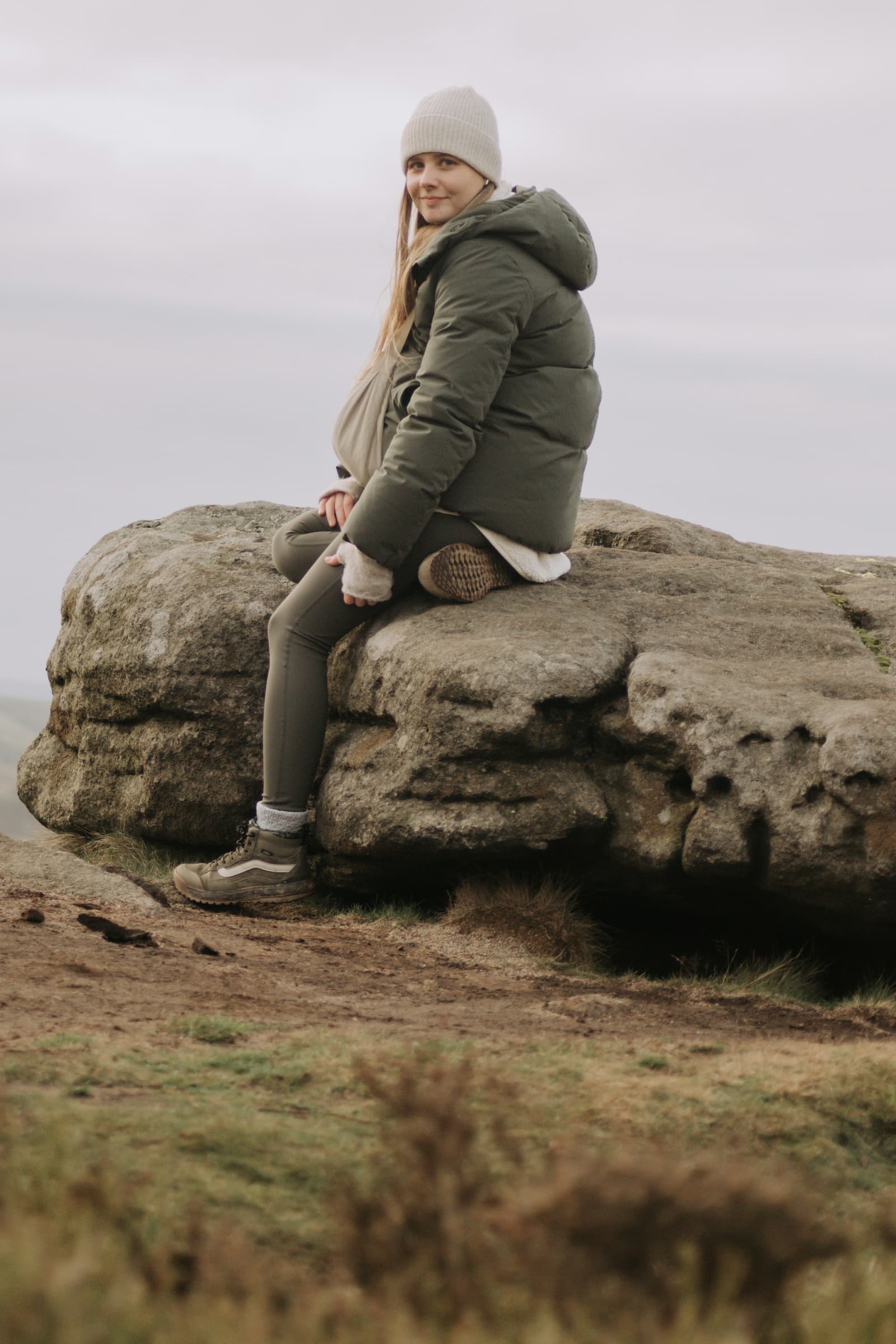 Woman in warm winter coat sitting on a rock outdoors