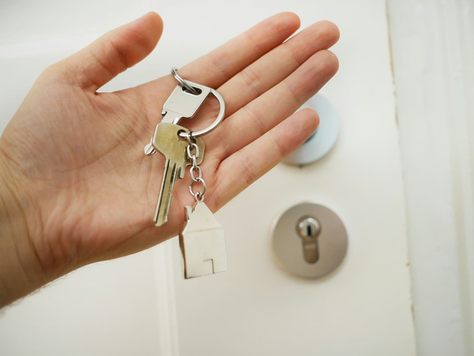 Hand holding house keys with house-shaped keychain by front door